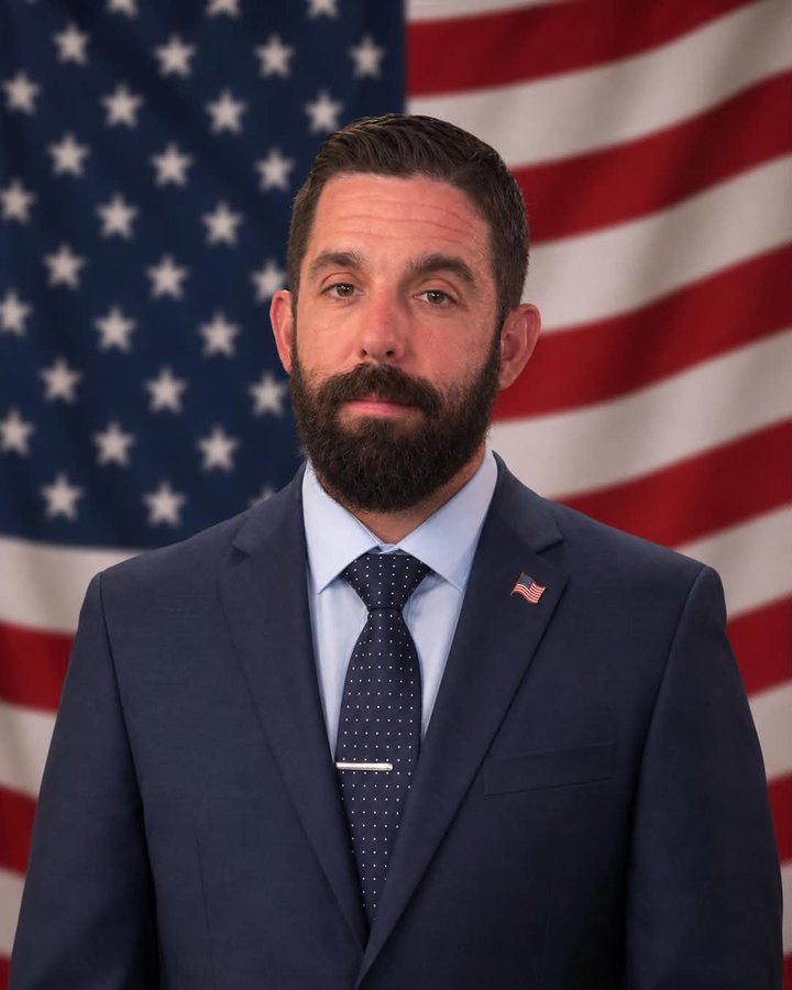 Donn Mann III, Director and Co-Founder of Veterans Resource Alliance, in a navy suit with a U.S. flag lapel pin and a U.S. flag behind him